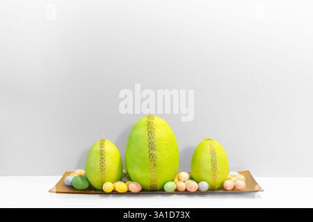 Simple and elegant white Easter background with Easter egg shaped green candles on the golden plate and dyed small quail colorful eggs laying around. Stock Photo