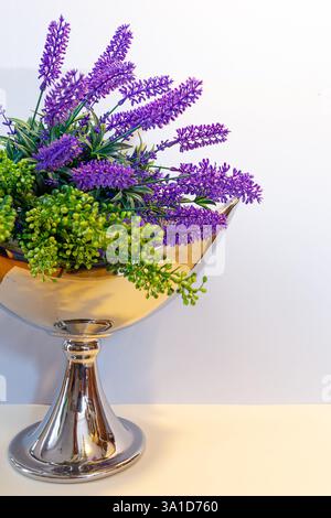 Lavender flowers bouquet composition in a golden vase on a table against white background, spring home decor. Stock Photo