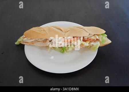 A sandwich is on a white plate. The sandwich is cut in half and has lettuce and tomato on it Stock Photo