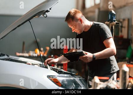 Using the tablet. Man is works in the automobile repairing salon. Stock Photo