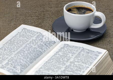 Black coffee in a white cup on a black saucer with a book and morning essentials on the table. Stock Photo