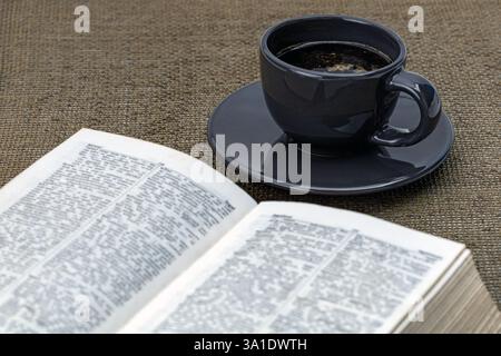 Black coffee in a black cup on a black saucer with a book and morning essentials on the table. Stock Photo