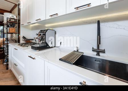A kitchen sink with a coffee maker on top of it. The sink is black and the coffee maker is silver Stock Photo