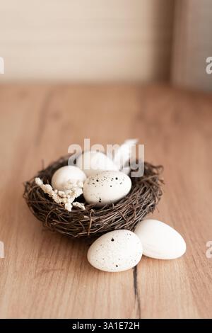 A beautiful Easter nest with three white eggs rests on a wooden surface, decorated with delicate feathers and dried flowers. The rustic style and soft Stock Photo