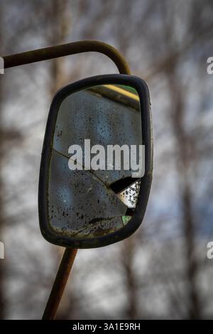 Close-up of a cracked, dirty tractor mirror reflecting tree branches that blend with the background Stock Photo