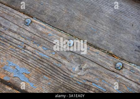 Abstract shot of old wood planks with peeling blue paint, held together by rusted iron nuts, from beneath a wooden boat Stock Photo