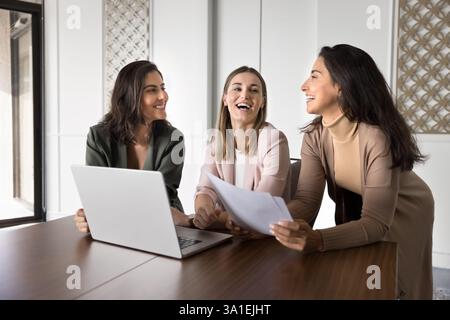 Three multiracial women colleagues distracted for work, joking and giggling Stock Photo