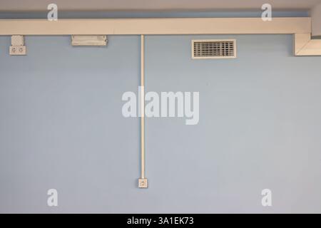 Minimalism and symmetry in the interior. Wiring, ventilation, lighting on the blue wall Stock Photo