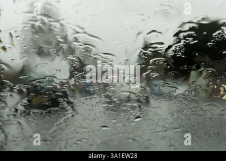 Abstract close up view of rain on a car windscreen, with town traffic in the background, UK. Stock Photo
