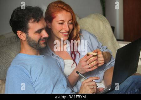 man and woman working at home on laptop computer talking and smiling Stock Photo