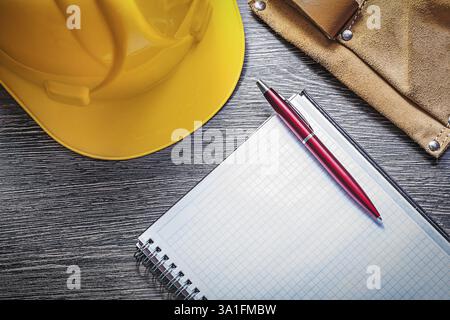 Leather construction belt protective building helmet checked notepad pen on wooden board Stock Photo