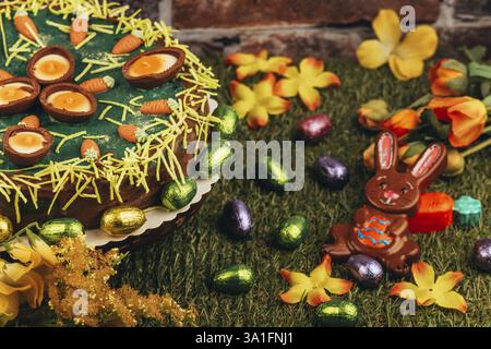 An Easter cake with carrots next to chocolate eggs, Easter bunnies and flowers on green grass Stock Photo