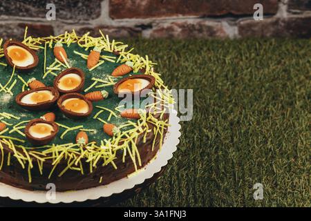 An Easter cake decorated with chocolate eggs and small carrots on green grass Stock Photo