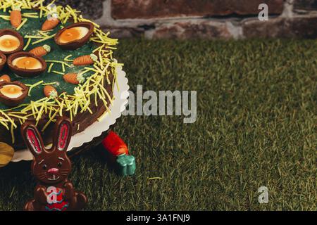Easter cake decorated with chocolate eggs and small carrots on green grass with an Easter bunny Stock Photo