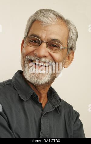 South Asian Indian old man late fifties with gray hair and beard wearing dark blue shirt and spectacles satisfyingly laughing MR#340 Stock Photo