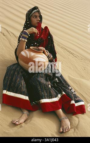 Rajasthani Woman holding clay pot sitting on sand and waiting, Bikaner, Rajasthan, India MR Stock Photo