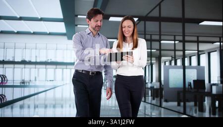 Happy Workplace Conversation: Two colleagues walk and talk with tablet Stock Photo