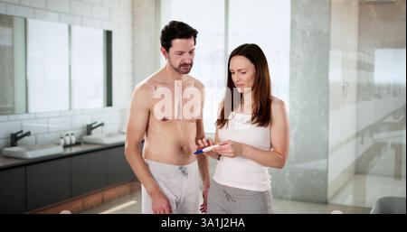 Surprised young couple examining pregnancy test results in bathroom at home. Stock Photo