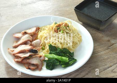 dry Chinese egg yellow noodles with red barbecue pork and dumpling on plate with clear soup cup Stock Photo