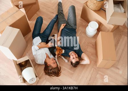 View from the top, lying down and resting. Young couple with dog are moving to new home. Stock Photo