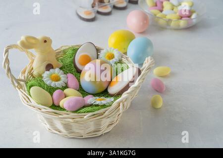 Spring easter basket preparation. Easter sweets and pastel colored eggs on white marble stone table. White chocolate bunny, marzipan and chocolate alm Stock Photo