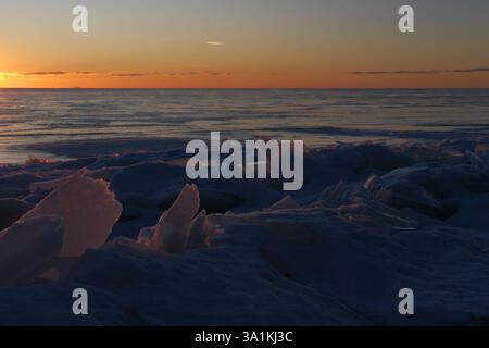 Shattered ice formations and shards on a frozen shoreline at sunset. Sharp ice floes frozen into coastline of Baltic sea in winter Stock Photo