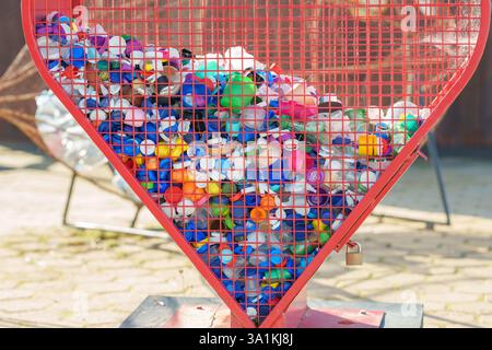 Altura, Portugal, February 19, 2025. Recycling bin shaped like a heart filled with plastic bottle caps in various colors. Stock Photo