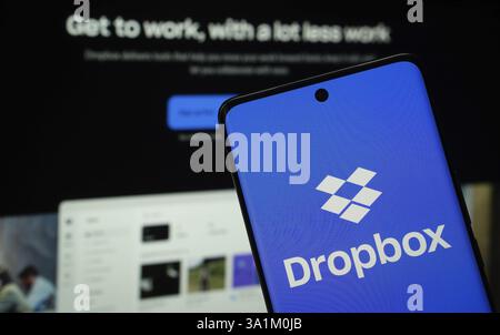 Dropbox logo is displayed on a smartphone screen, with the dropbox website visible on a computer screen in the background Stock Photo