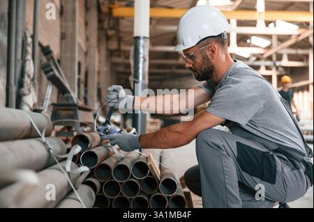 Sitting and working. Young man at the factory in grey uniform. Stock Photo