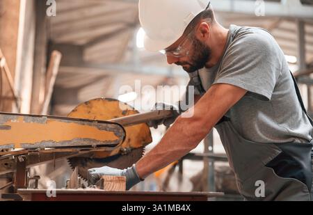 Sitting and working. Young man at the factory in grey uniform. Stock Photo