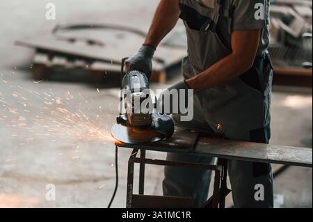 Using angle grinder. Close up view of man that is working at the factory. Stock Photo