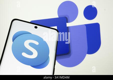 Skype logo is displayed on a smartphone screen, with the microsoft teams logo visible on a computer screen in the background Stock Photo
