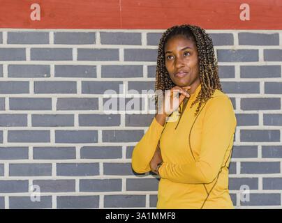 Young black woman in yellow with curly hair posing against a brick wall, Taken in Daejeon, South Korea, Asia Stock Photo
