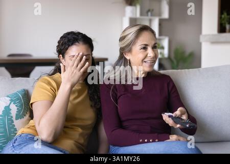 Young woman sitting on couch, watching television with older mother Stock Photo