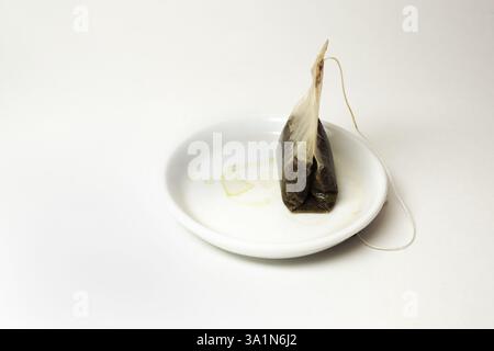 used tea bag with a long thread, on small white saucer with tea stains Stock Photo