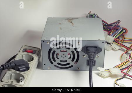 computer ATX non-modular power supply unit, with connected power cord. switch on surge protector. old power connectors for drives Stock Photo
