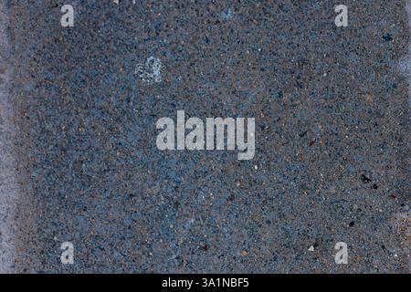 A close-up shot of weathered asphalt with small rocks and discoloration. Primarily gray-blue with some light-colored flecks and edges. Stock Photo