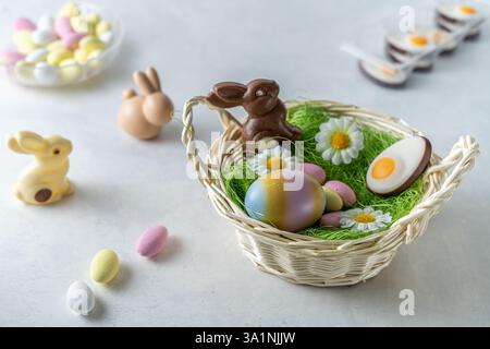 Chocolate Easter bunny in basket. pastel colored almond sweets and eggs on white marble stone table. Light and airy, high angle view, copy space Stock Photo
