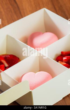 Gift set of heart-shaped mousse cakes and shortbread baskets with strawberries in a box. Cardboard box with cakes on a table in a cafe, selective focu Stock Photo