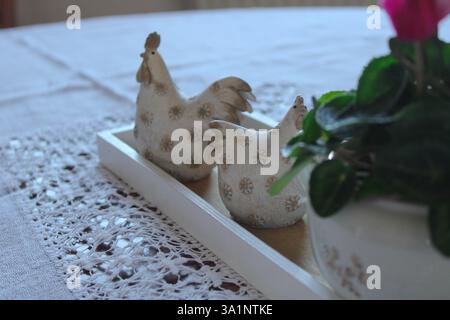 Rustic farmhouse table decor with ceramic hen figurines on a wooden tray, placed on a lace tablecloth, creating a cozy country-style ambiance. Stock Photo