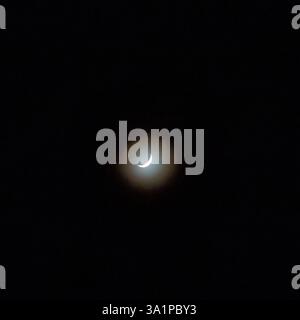A luminous crescent moon surrounded by a soft halo against a deep black night sky, creating a serene and mysterious atmosphere. Stock Photo