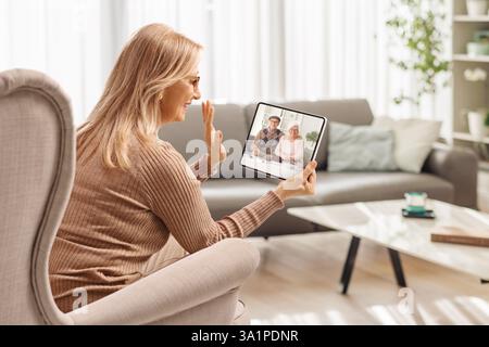 Woman sitting in an armchair and making a video call with elderly parents on a digital tablet at home Stock Photo