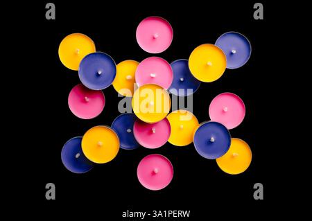 Tea lights in pink, yellow, and blue, arranged in a playful composition against a stark black backdrop. Stock Photo