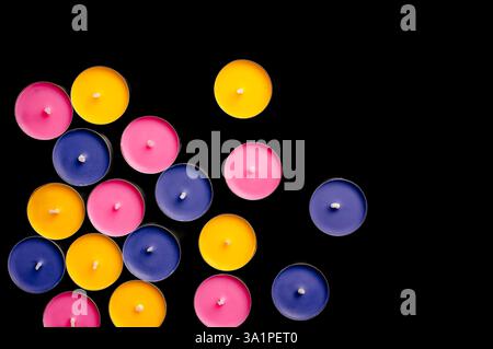 Tea lights in pink, yellow, and blue, arranged in a playful composition against a stark black backdrop. Stock Photo