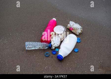 A bottle of water is laying on the beach next to other bottles and plastic cups. The scene is littered with trash, and it's clear that the beach is no Stock Photo
