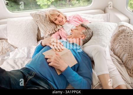 Happy mature woman and her husband relaxing on bed in motorhome during camping vacation Stock Photo