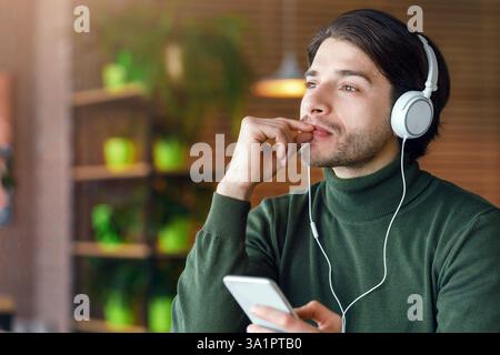 Pensive guy in headphones listening to music, using smartphone Stock Photo