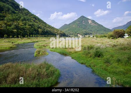 Sunchang County, South Korea - October 4, 2021: A winding stream flows into the Seomjin River, surrounded by lush grasslands and forested mountains un Stock Photo