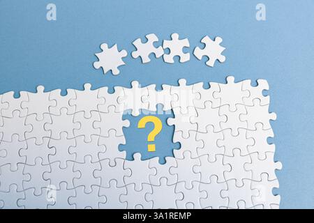 A white jigsaw puzzle on blue background. pieces is missing in the center, with a yellow question mark, four puzzle pieces placed above, Stock Photo