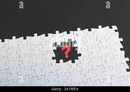 An incomplete jigsaw puzzle with a distinct absence of a red question mark piece on black background, highlighting a sense of mystery or inquiry Stock Photo